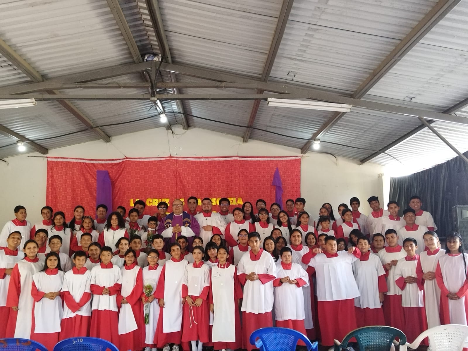 Grupo de acólitos con vestiduras rojas y blancas junto a un sacerdote frente al altar